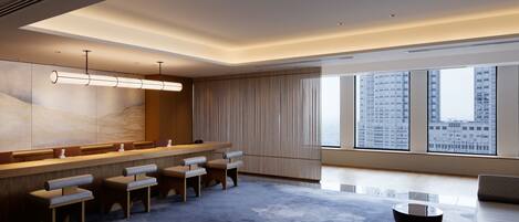 Un hall d’hôtel moderne doté d’un long comptoir d’accueil, d’un espace salon et de grandes fenêtres offrant une vue sur la ville.