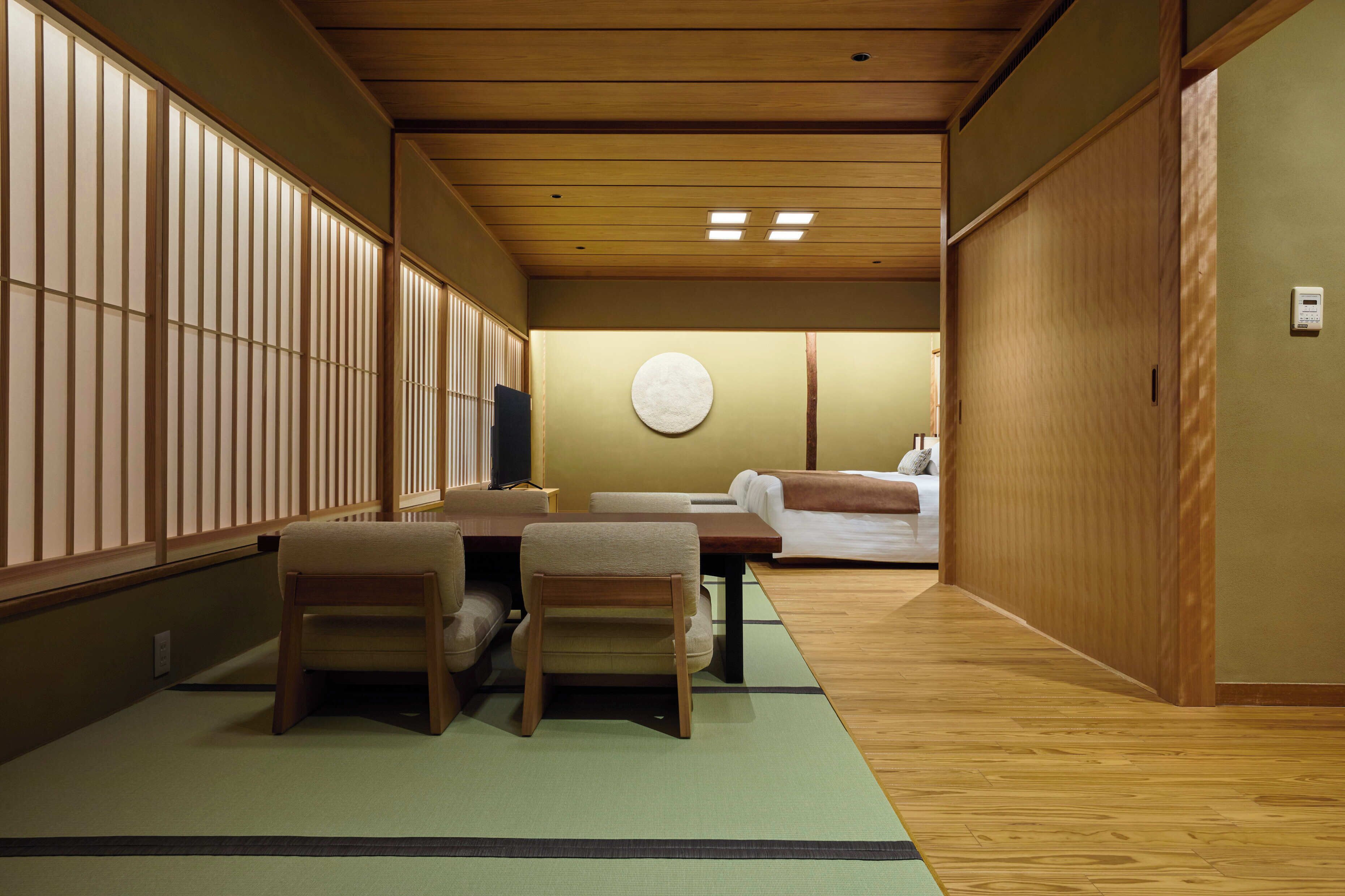 Una habitación japonesa tradicional con suelo de tatami, una mesa baja con sillas, un futón y puertas correderas.