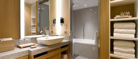 A modern bathroom with a large sink, a walk-in shower, and a vanity with a mirror.