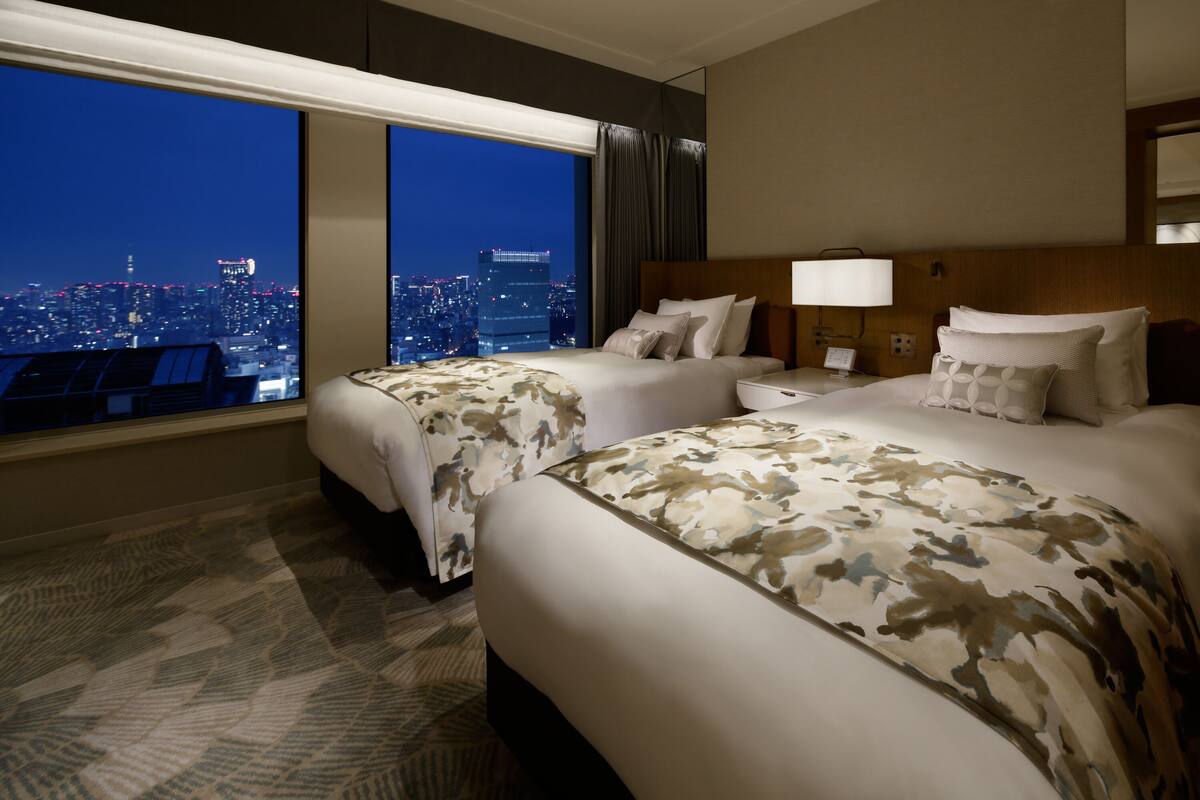 A hotel room with two beds, a city view, a large window, and a carpeted floor.