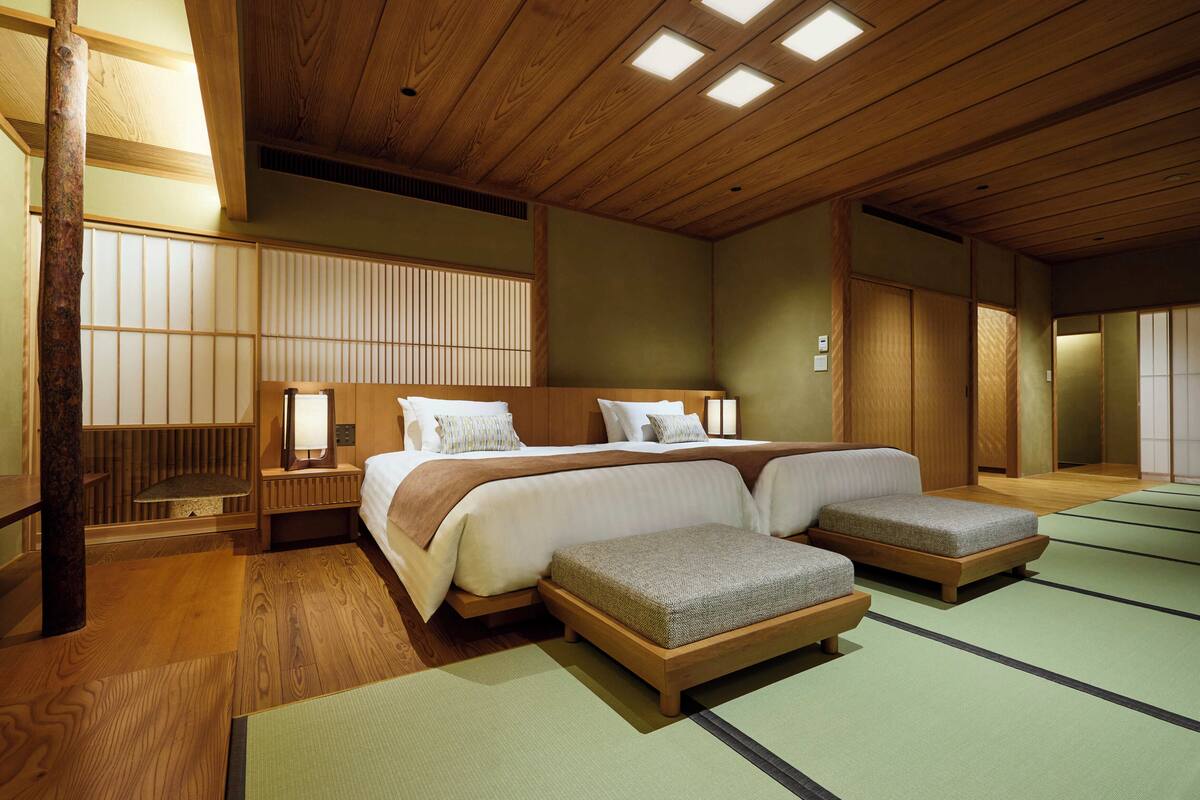 A traditional Japanese-style room with tatami flooring, a large bed with two pillows, a nightstand, and a wooden ceiling with recessed lighting.