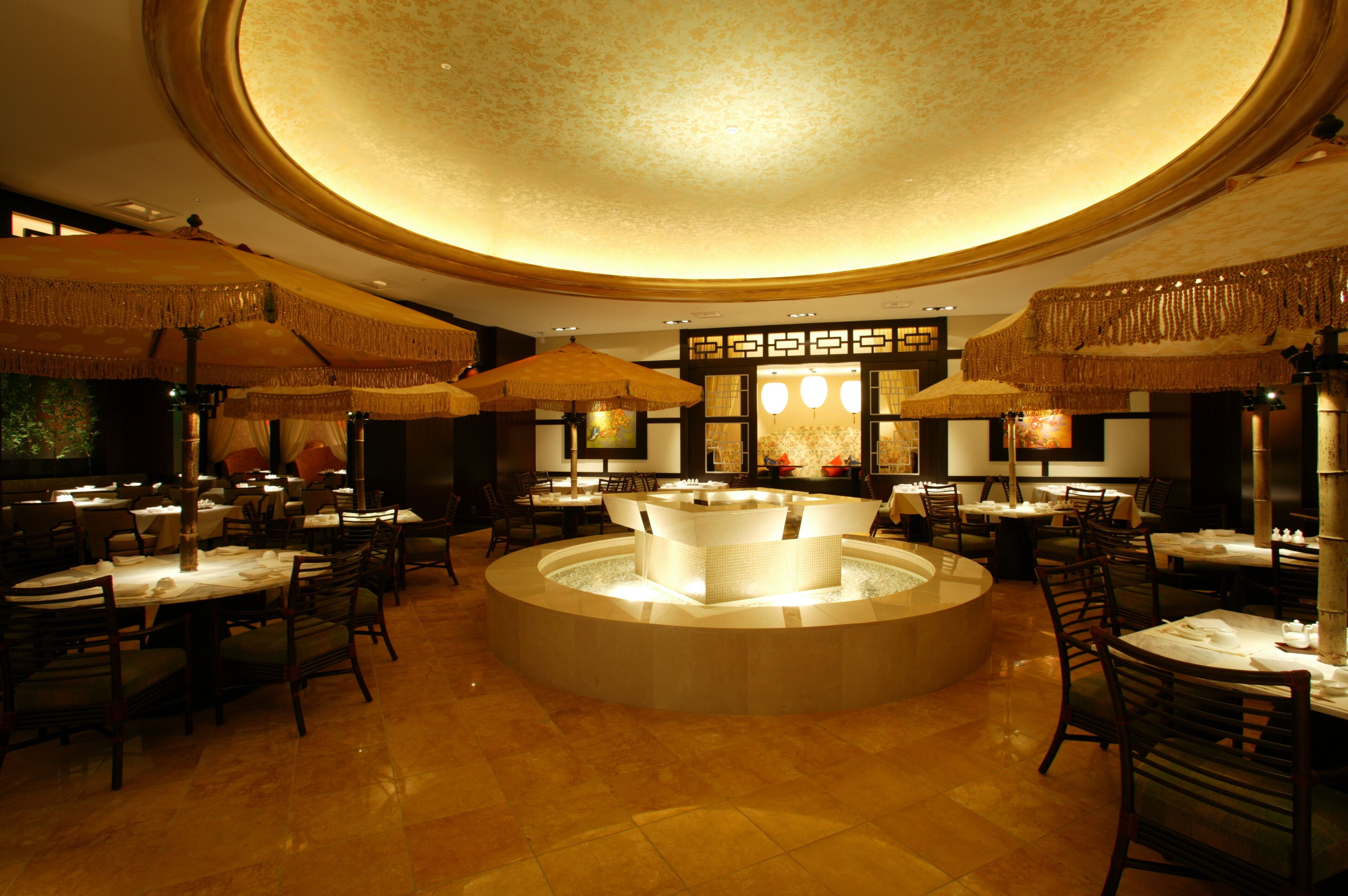 Een restaurant met ronde tafels, rieten parasols en een fontein in het midden.