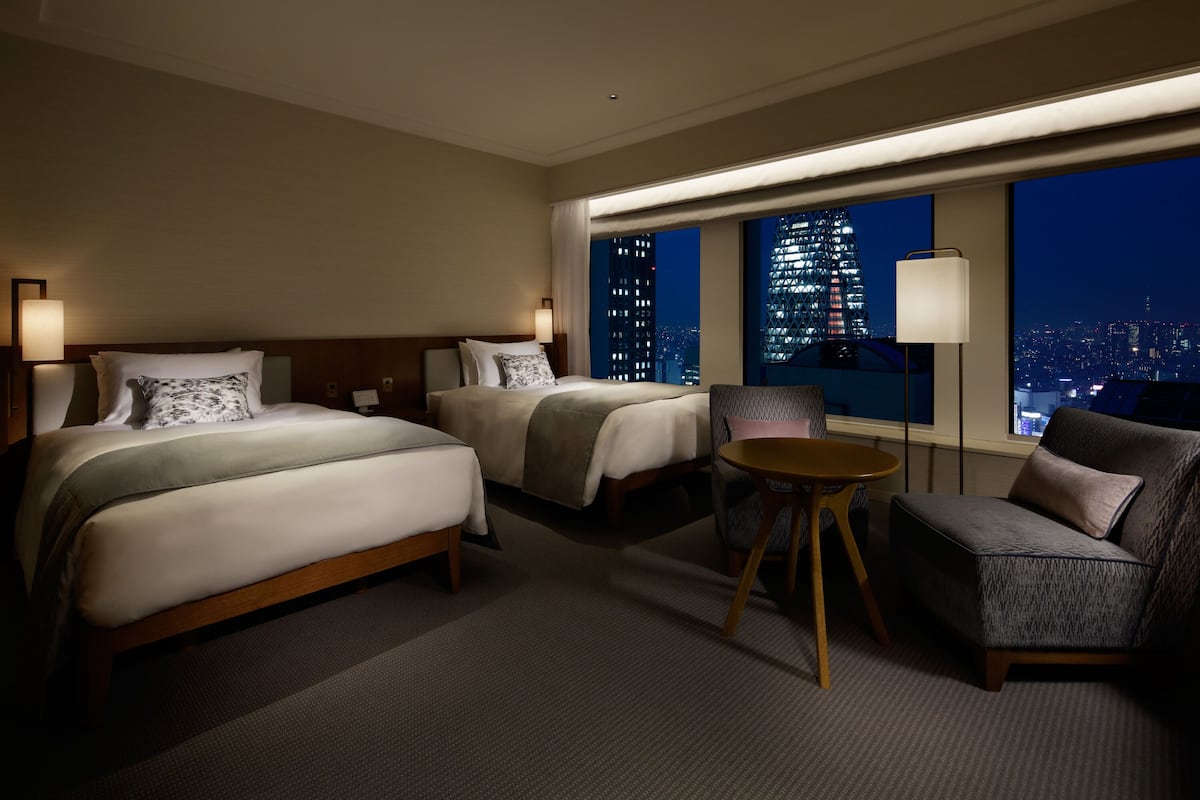 A hotel room with two beds, a sofa, a small table, and a city view.