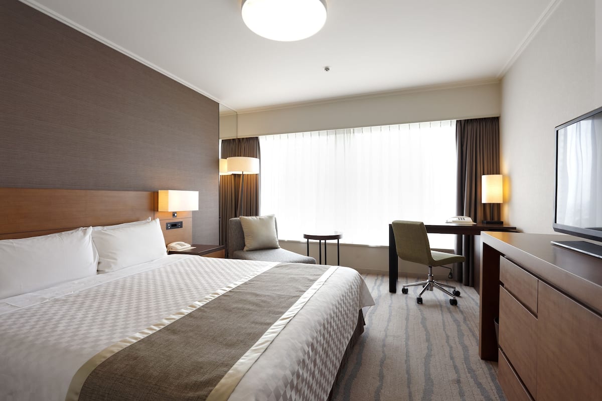 A hotel room with a large bed, a desk, a chair, and a television.