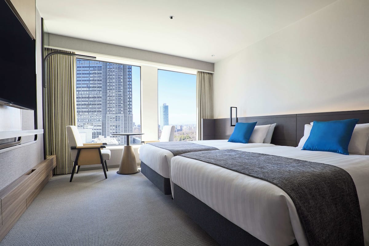 A hotel room with two beds, a TV, a chair, and a large window with a city view.