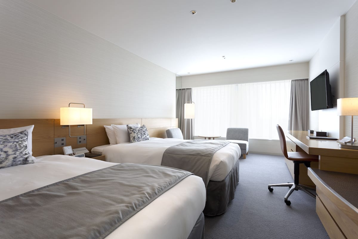 A hotel room with two beds, a desk, a chair, a television, and a window with curtains.