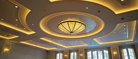 A spacious hotel room with large windows, a circular ceiling design, and recessed lighting.