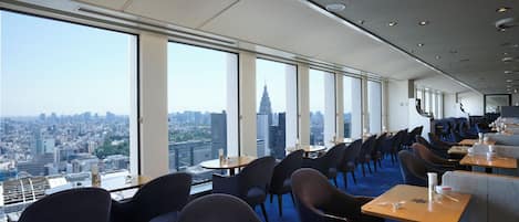 Un restaurante de altura con vistas panorámicas de la ciudad, asientos modernos y un interior amplio y luminoso.