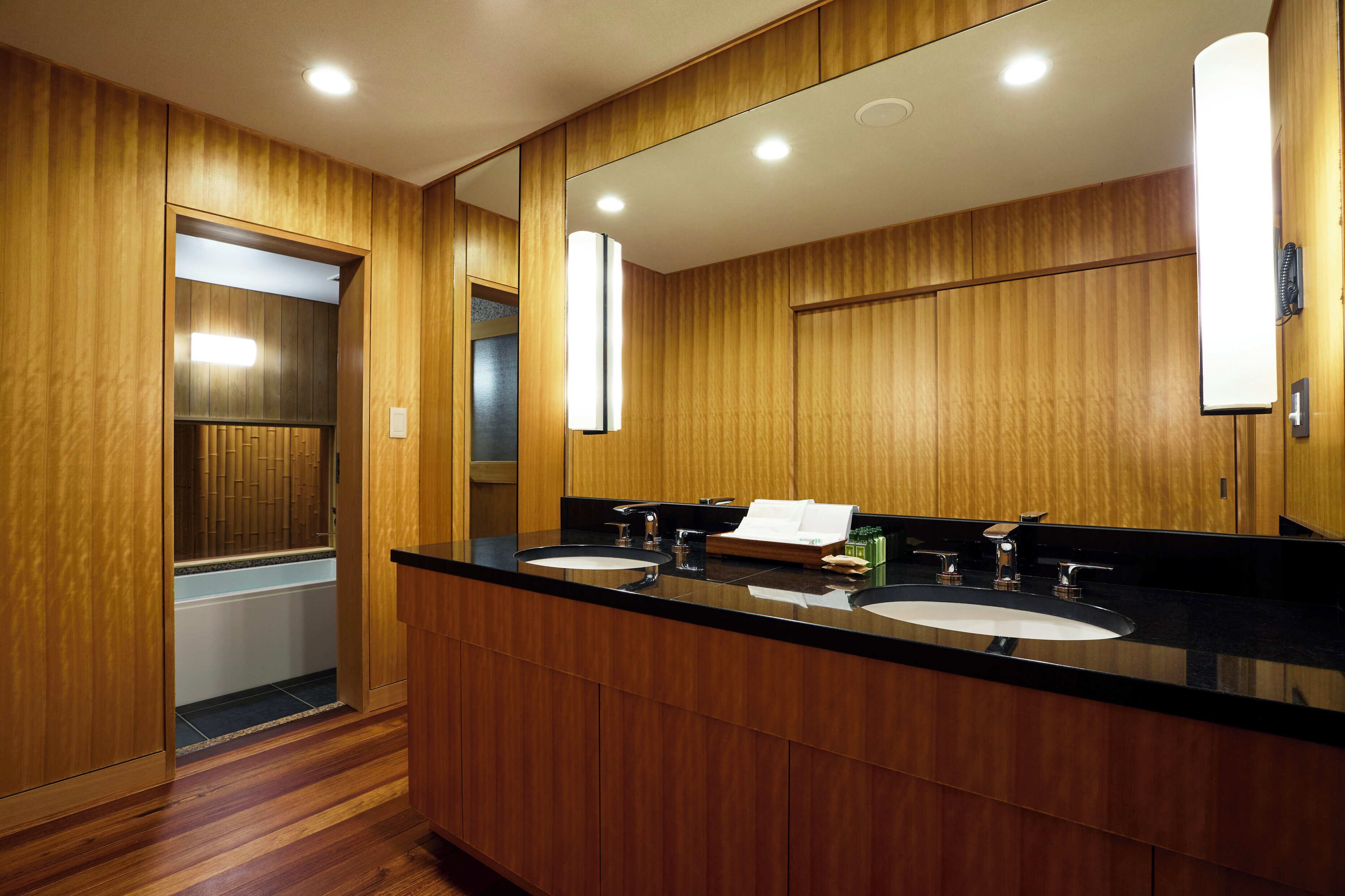 A hotel bathroom with wooden paneling, a large mirror, two sinks, and a towel rack.