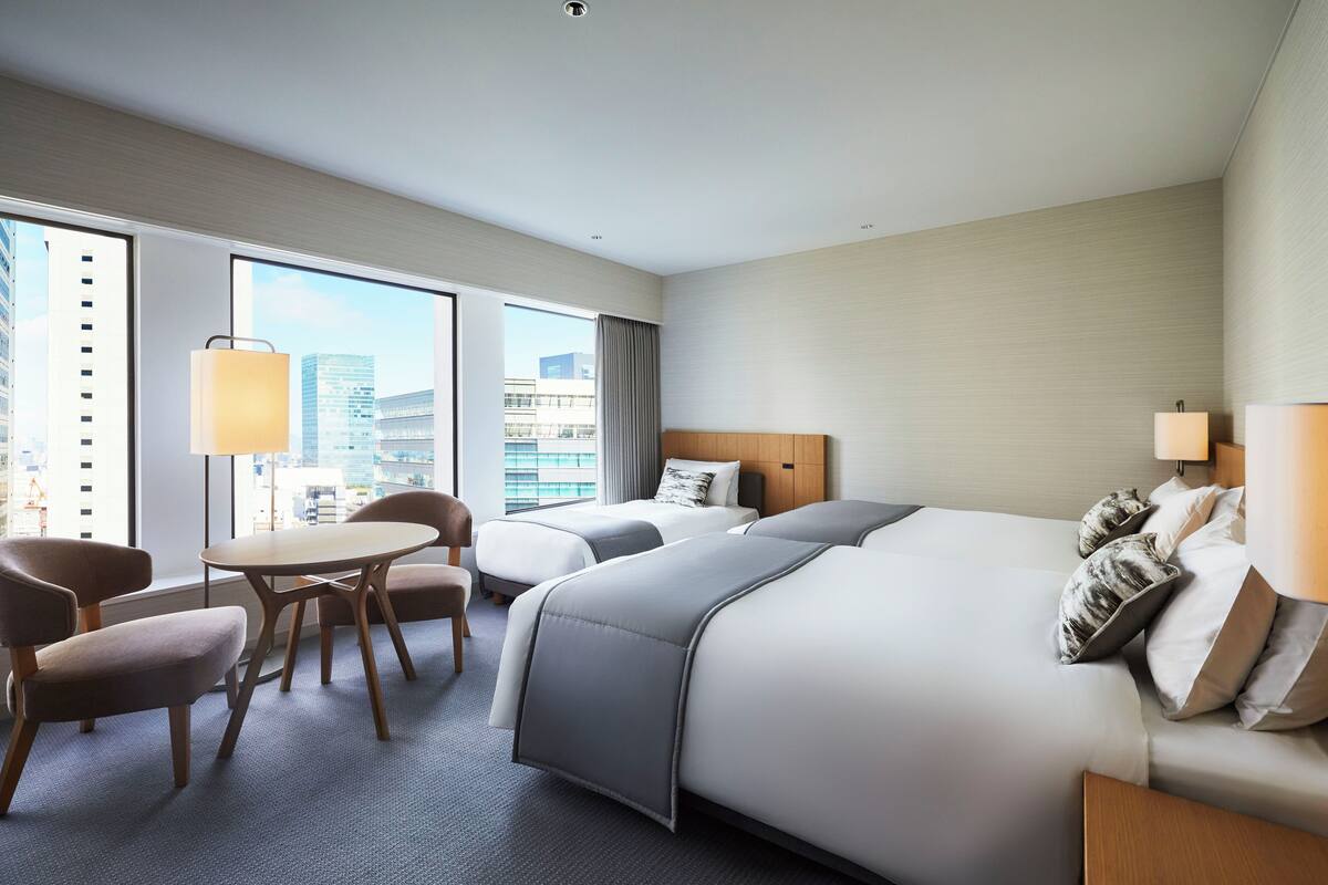 A hotel room with a large bed, a desk, two chairs, and a view of the cityscape.
