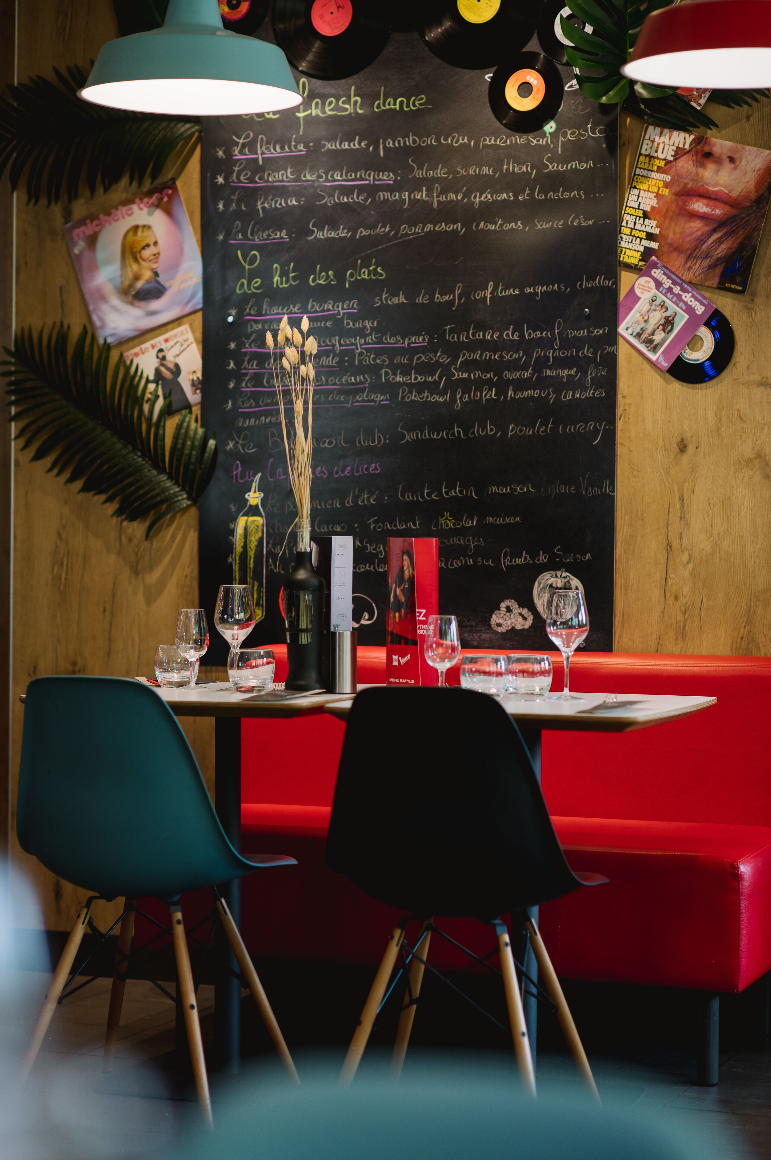 Een restaurantinterieur met een krijtbordmenu, vinylplaten en een rode zithoek.