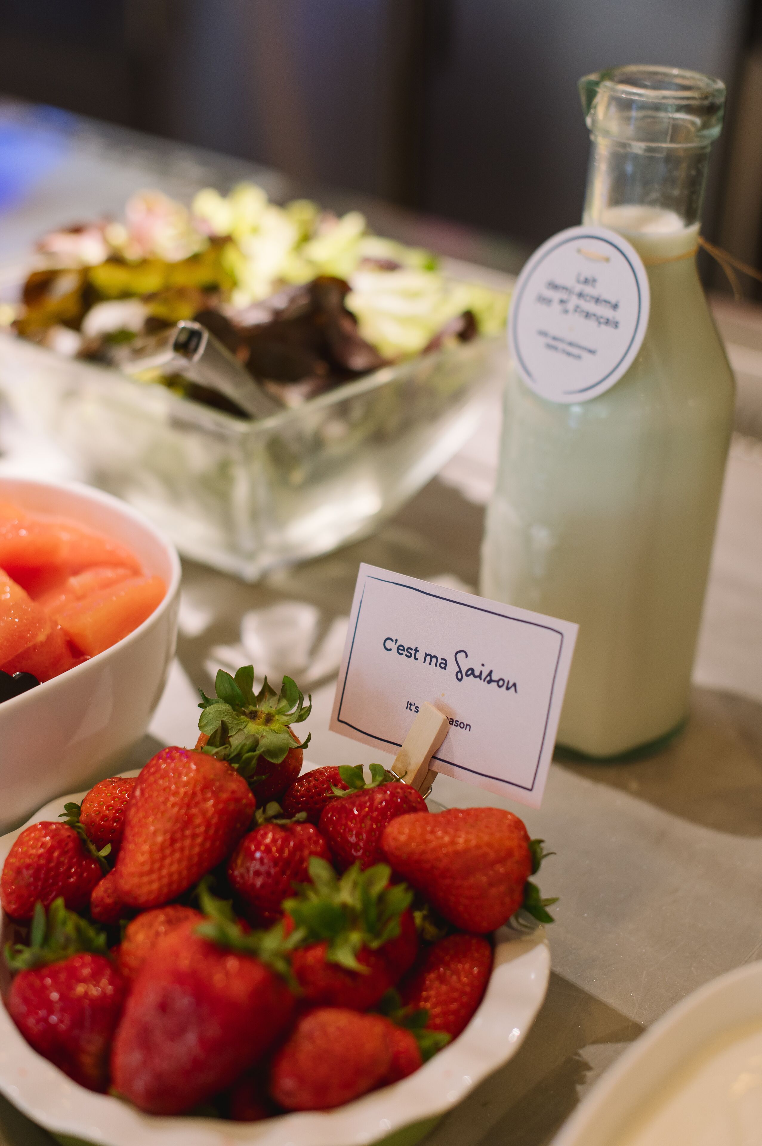 Una mesa con un bol de fresas, una botella de leche y un letrero que dice 'C'est ma Saïton'.