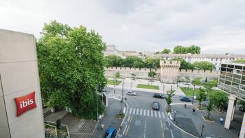 Vista de una intersección urbana con un edificio moderno que muestra el letrero rojo de 'ibis', un paso de peatones y un coche azul en primer plano.