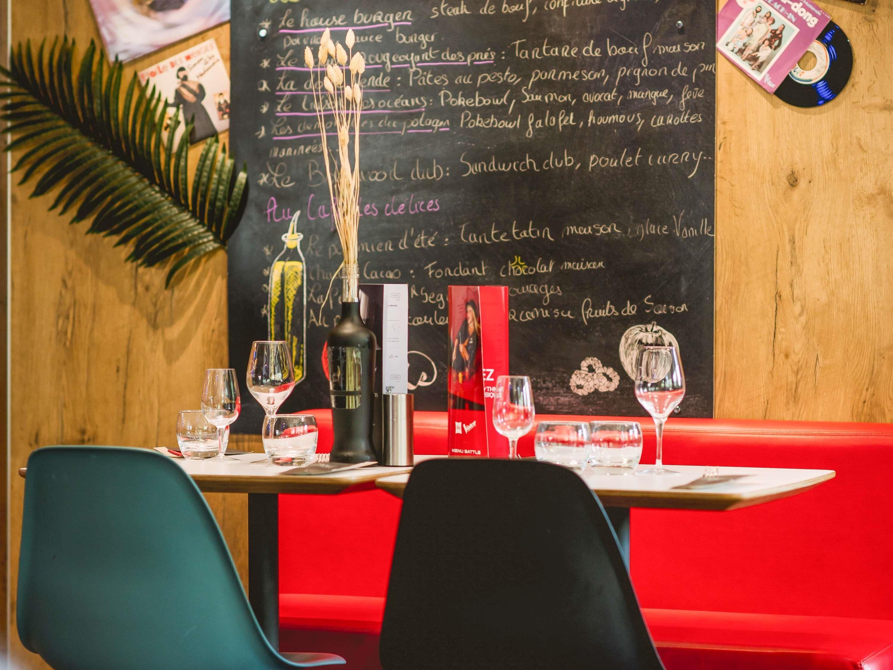 A restaurant interior with a chalkboard menu, wine glasses, a bottle, and a menu board on a table.