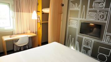 Habitación de hotel con cama, escritorio, silla, televisor y un pared con dibujos en la pizarra.