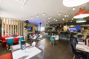 A restaurant with a bar area, multiple seating options including booths and tables, and a variety of lighting fixtures. - ibis Avignon Centre Gare (Avignon)