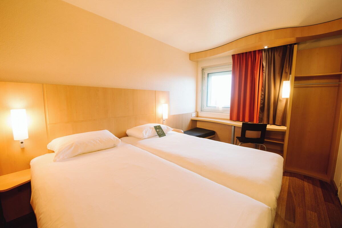 A hotel room with two beds, a desk, and a chair.
