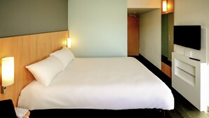 A hotel room with a large bed, bedside lamps, a TV, and a wooden headboard. - ibis Avignon Centre Gare (Avignon)