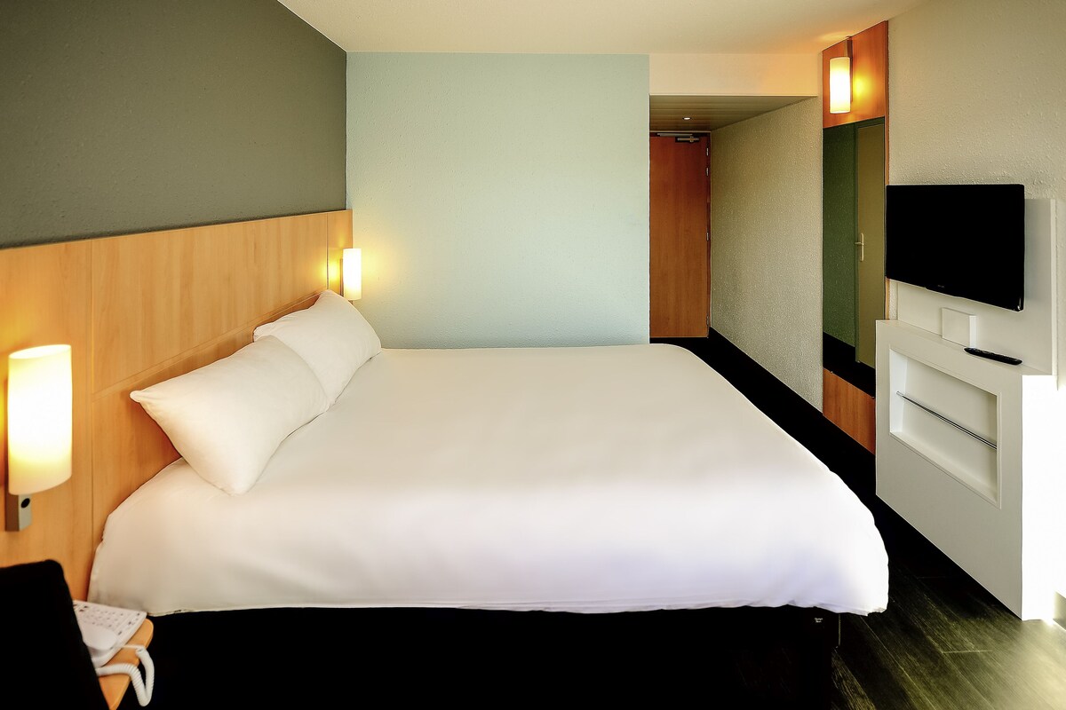 A hotel room with a large bed, bedside lamps, a TV, and a wooden headboard.