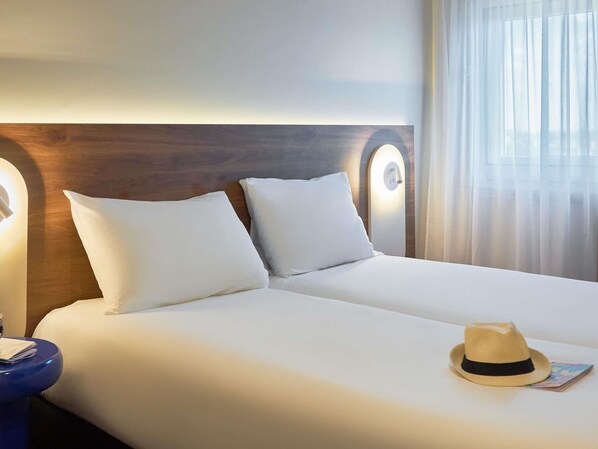 A hotel room with a bed, pillows, a nightstand, a hat, and a magazine. - ibis Avignon Centre Gare (Avignon)