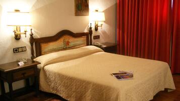 Habitación de hotel con una cama grande, dos mesitas de noche con lámparas, una cortina roja y un cuadro en la pared.