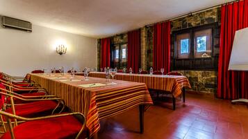 A conference room with tables set for a meeting, red chairs, and a stone wall with windows.