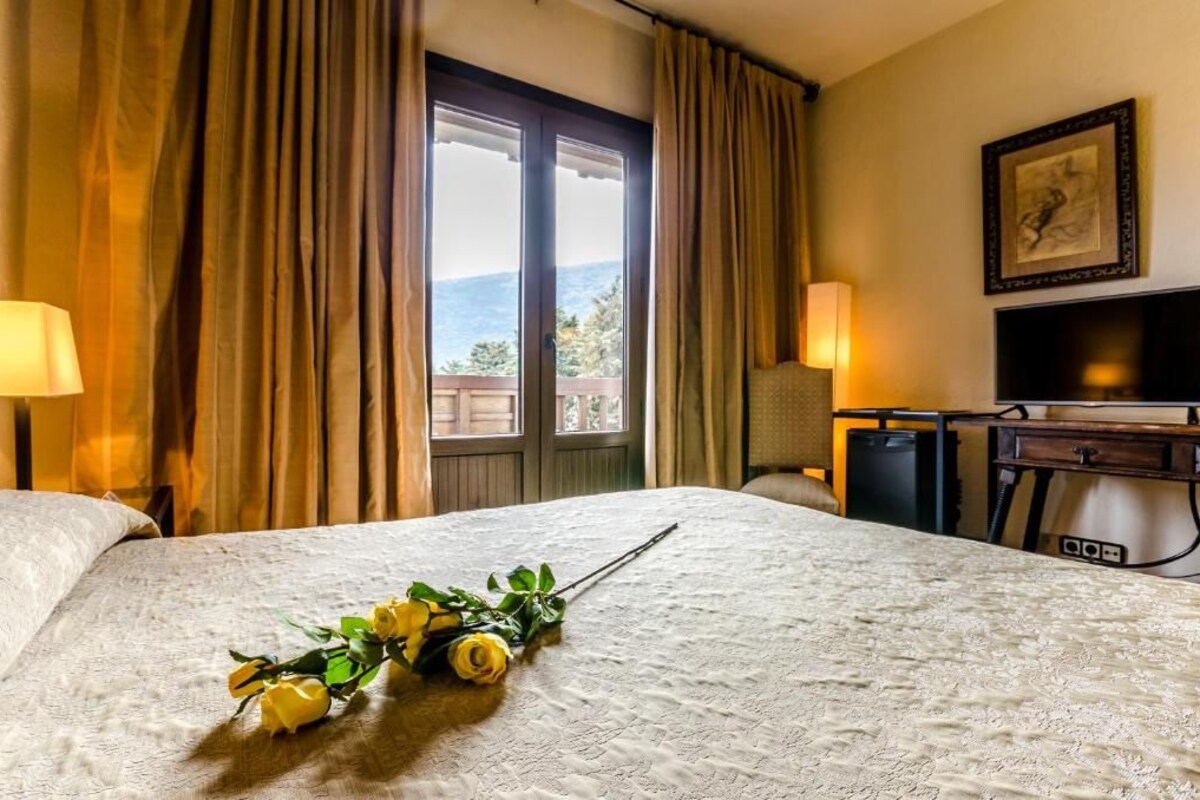 A hotel room with a large bed, a desk with a computer, a TV, and a view of the outdoors.