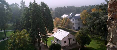 A large building with a white facade and multiple roofs, surrounded by trees and a well-maintained lawn.