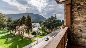 A balcony with a stone wall and a view of a street with cars and a hill in the background. - Hotel Temple Ponferrada (Ponferrada)