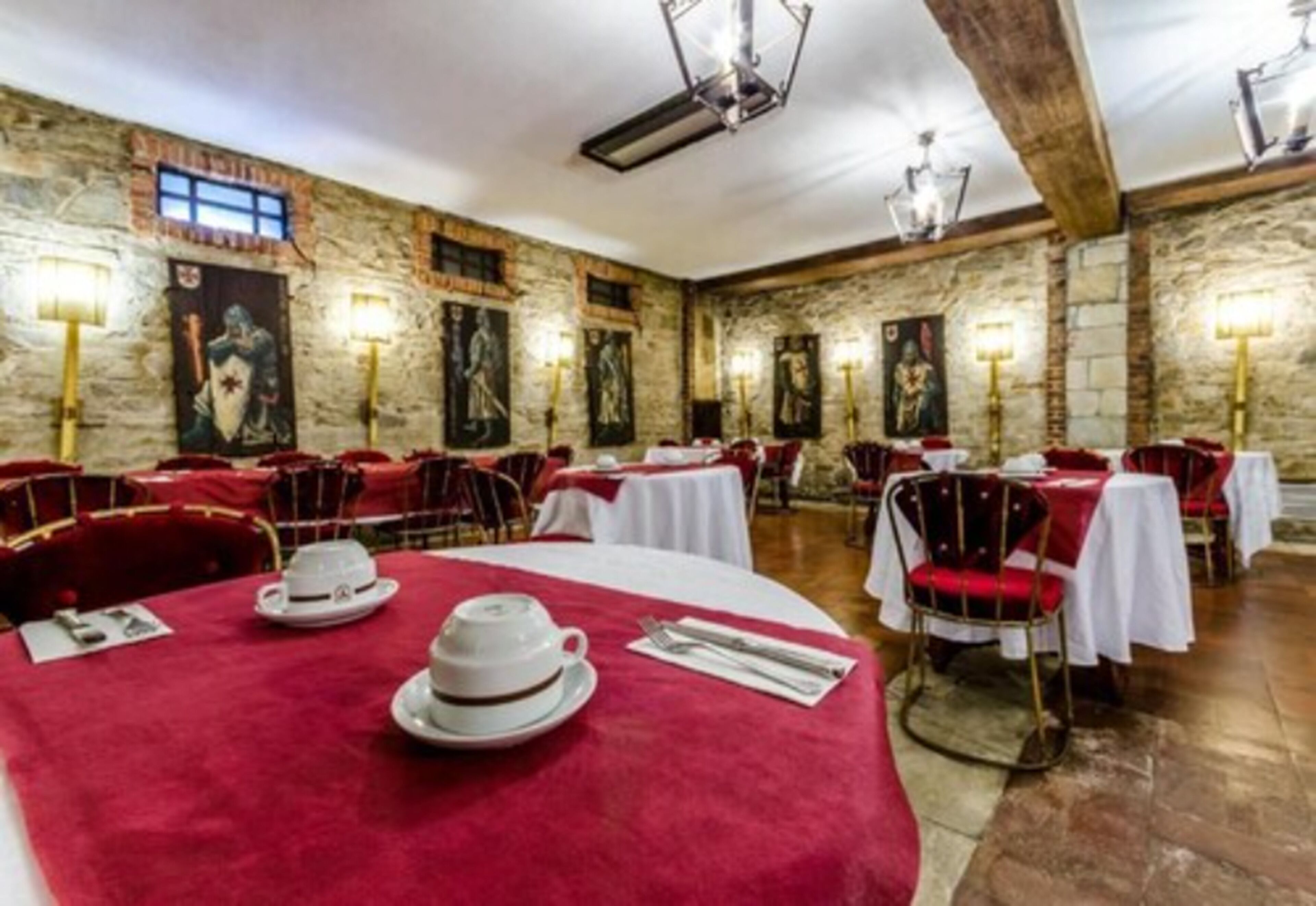 A restaurant with stone walls, red velvet chairs, and white tablecloths.