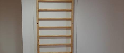Une échelle en bois adossée à un mur blanc, dans une pièce dont le sol est en bois.