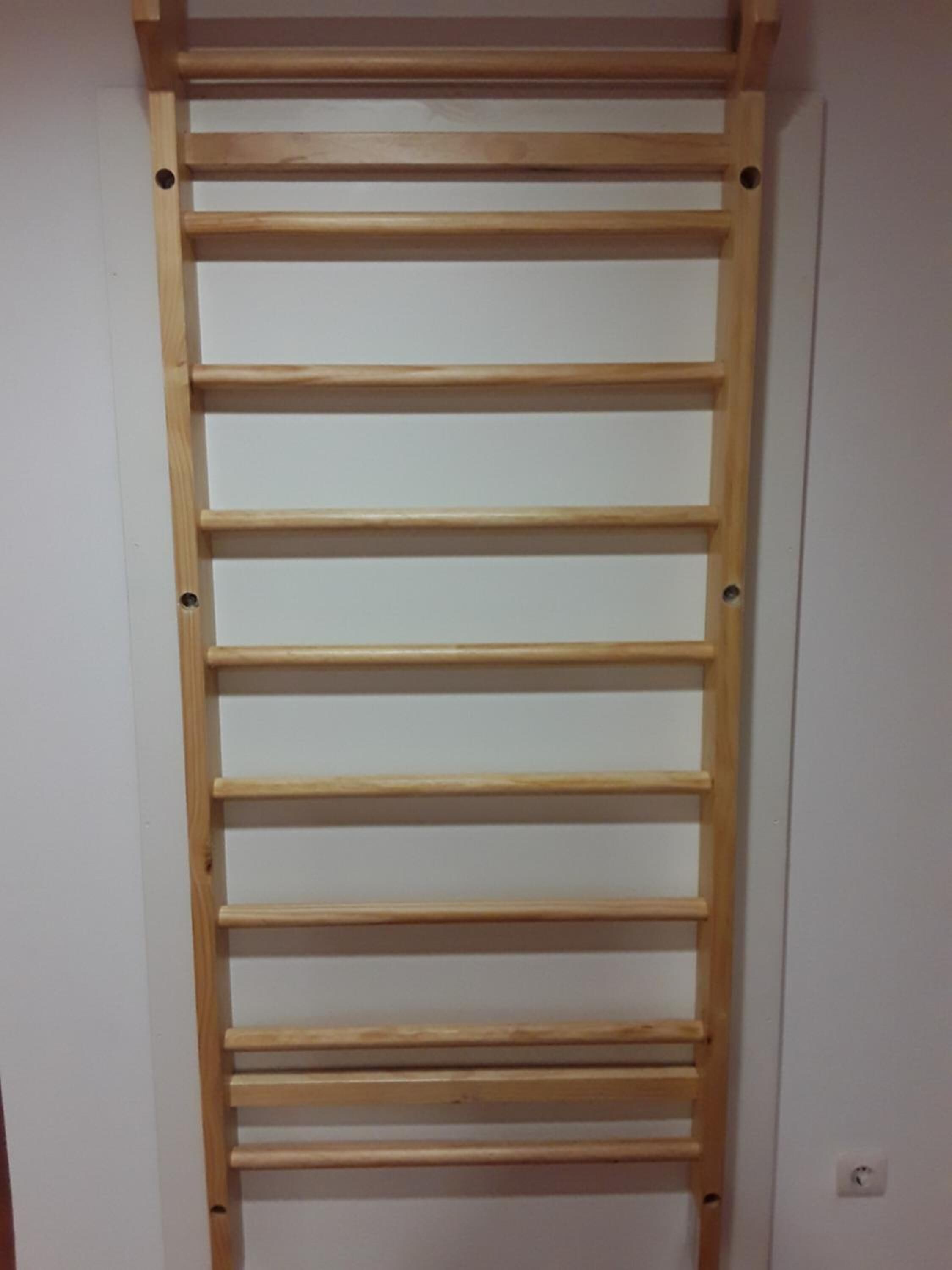 A wooden ladder with evenly spaced horizontal bars against a plain wall.