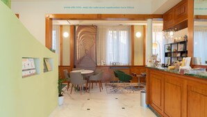 Un hall d’hôtel doté d’un escalier central, d’un comptoir d’accueil et d’un espace détente avec des fauteuils et une table.