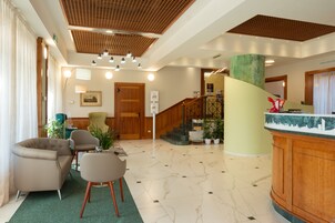 Una hall d'albergo con reception, una scala e un'area salotto.