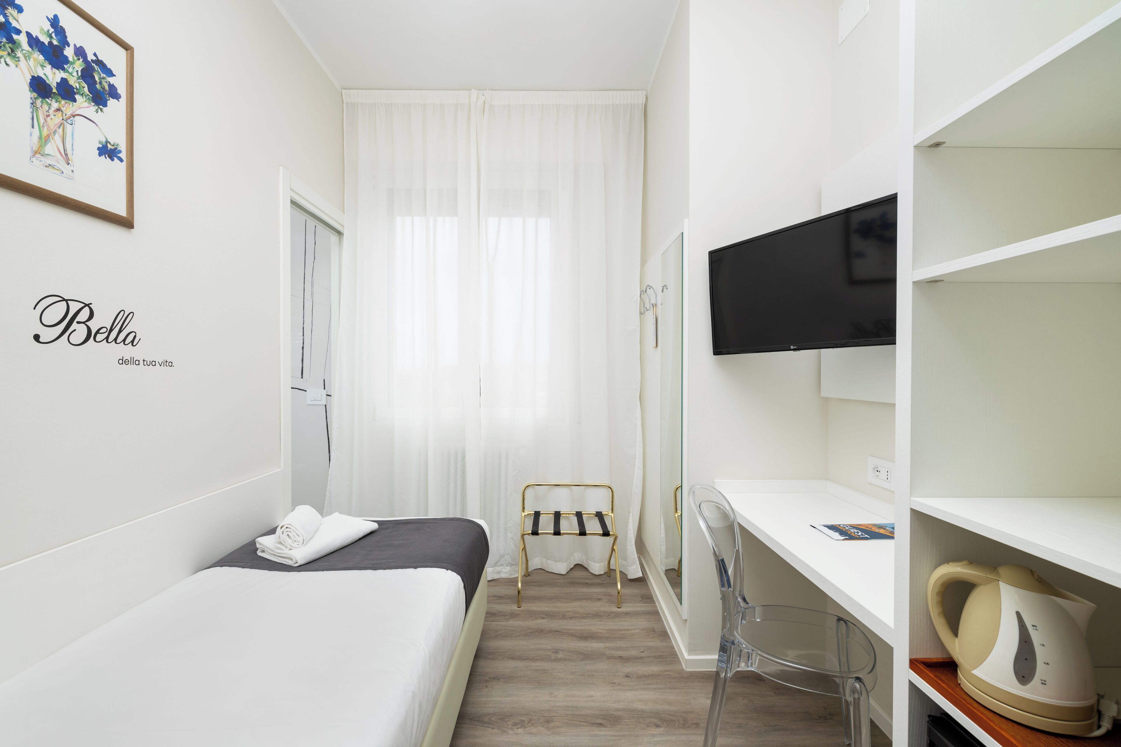 Une chambre d’hôtel équipée d’un lit, d’un bureau, d’une chaise, d’une télévision et d’une étagère avec une bouilloire.