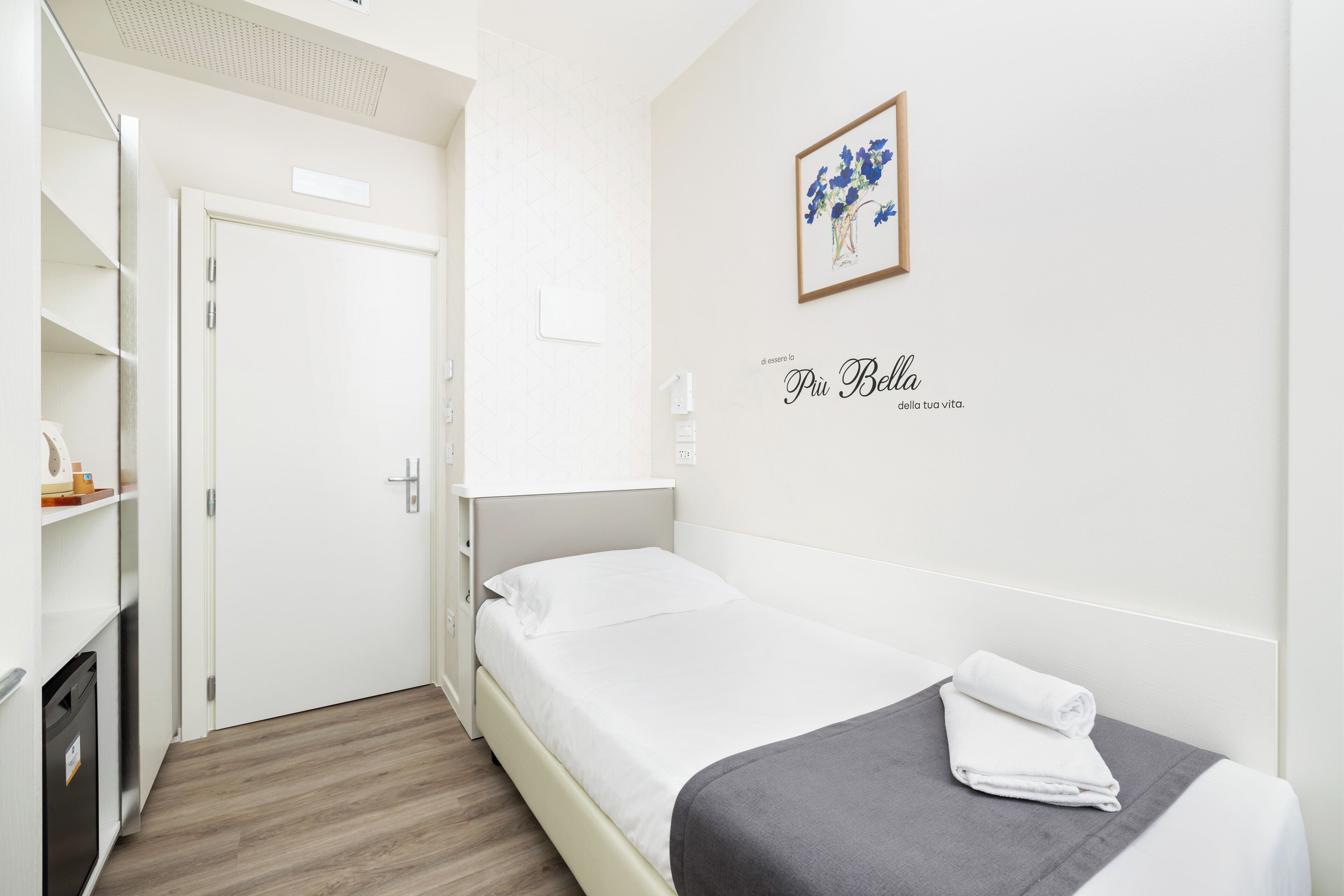 Ein kleines, ordentliches Schlafzimmer mit Bett, Nachttisch, Wandbild und einer Tür zum Badezimmer.