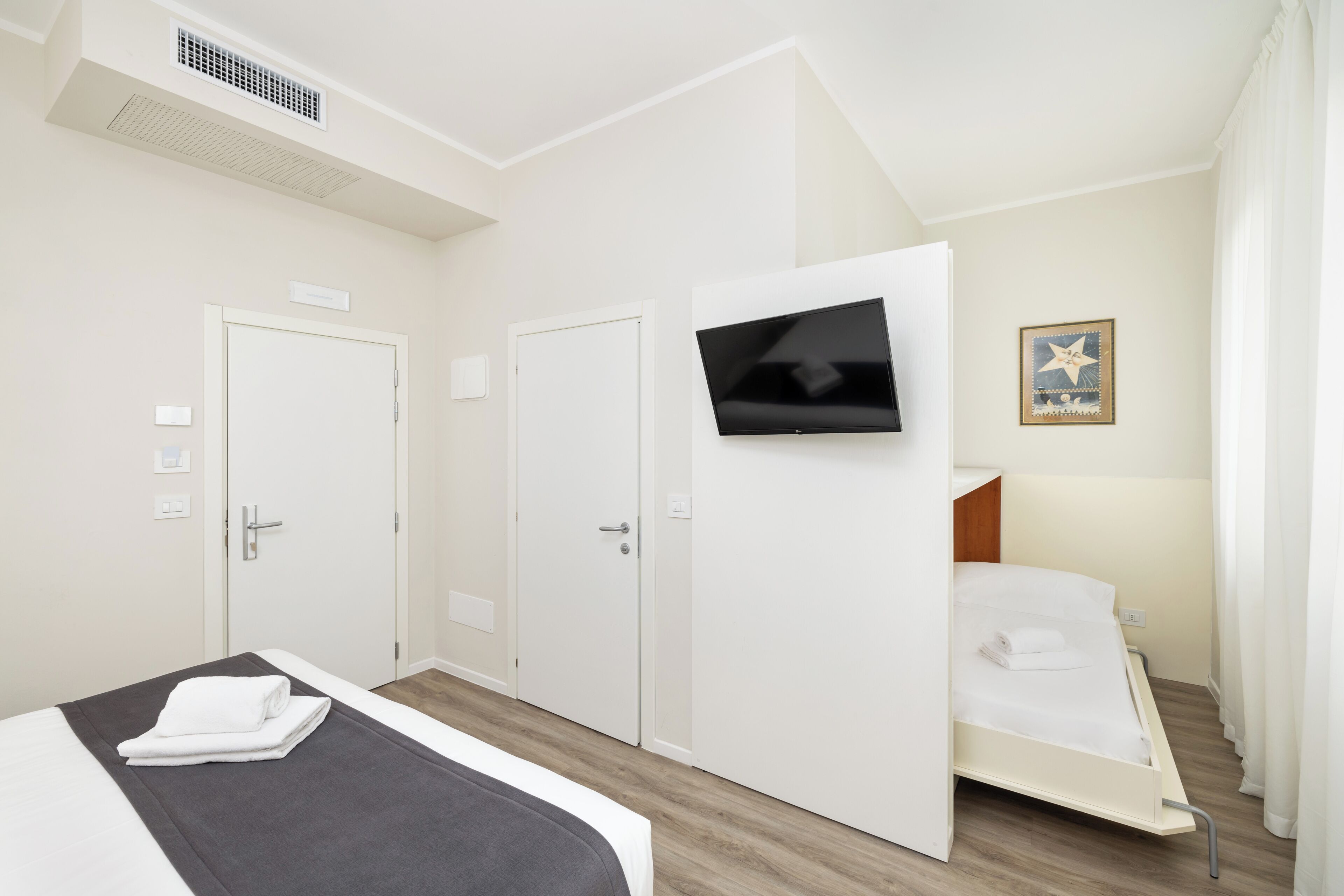 Una camera d'albergo con un letto, una TV a parete e una porta.