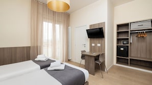 Une chambre d’hôtel avec deux lits, un bureau, une chaise, une télévision, une armoire et un radiateur.