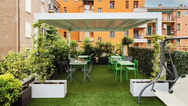 Une terrasse extérieure avec des chaises et des tables vertes, entourée de jardinières et surmontée d’un auvent blanc.
