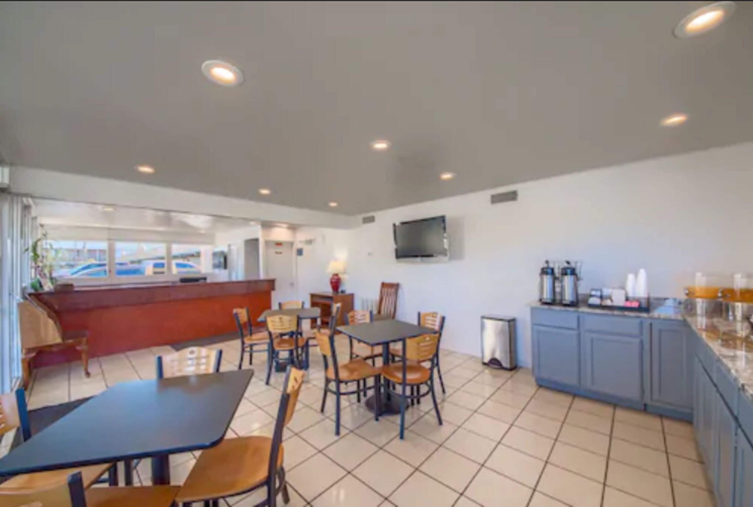 Un comedor con mesas y sillas, una cocina con armarios y electrodomésticos, y un televisor montado en la pared.