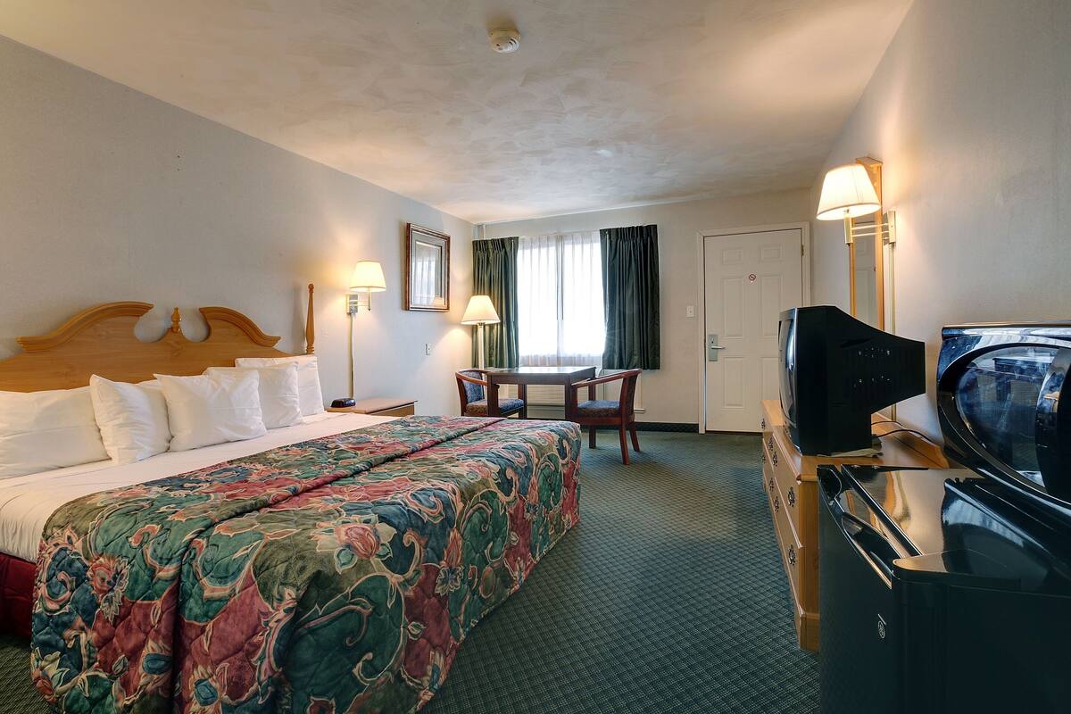 A hotel room with a large bed, a desk, a television, and a wardrobe.