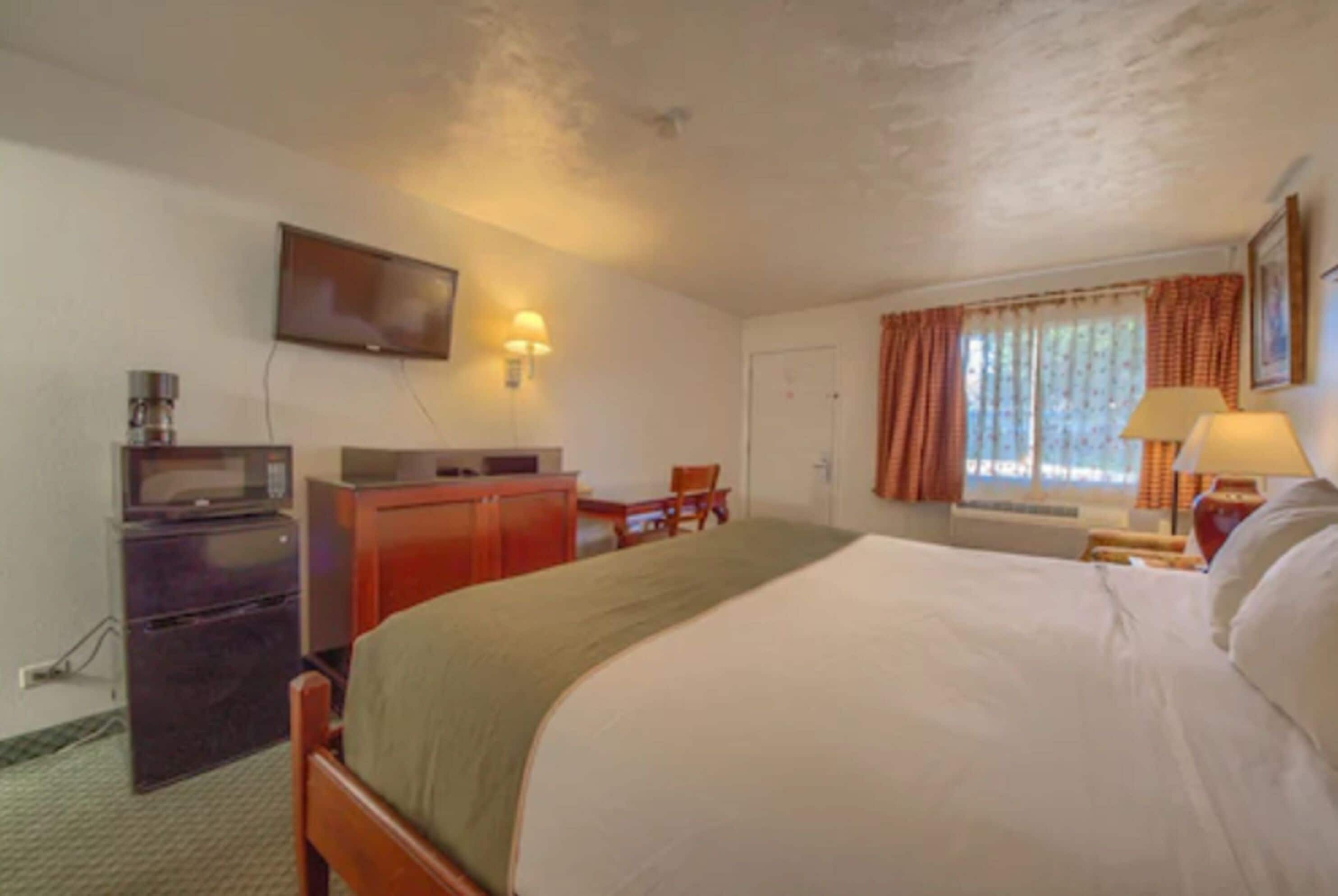 A hotel room with a bed, a desk, a television, and a window with curtains.