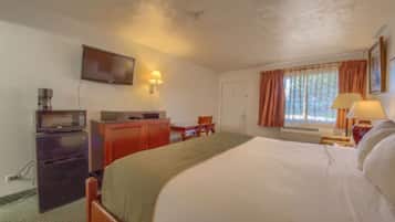 A hotel room with a bed, a desk, a television, and a window with curtains.