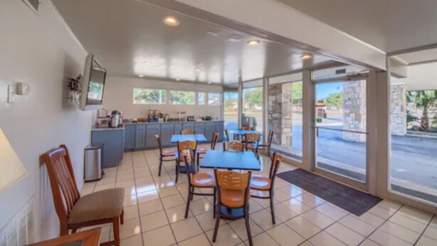 A spacious dining area with a kitchen in the background, large windows, and a view of the outside. - Americas Best Value Inn Uvalde (Uvalde)