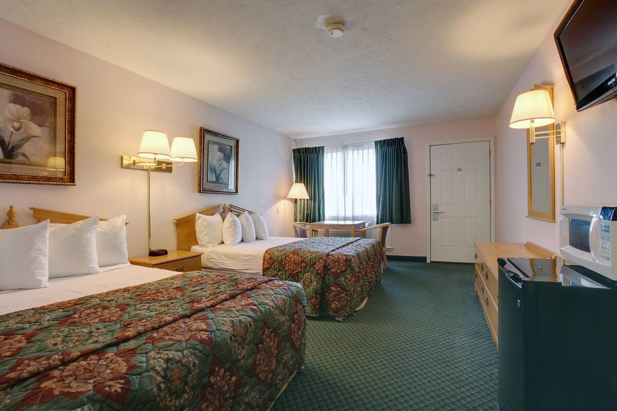 A hotel room with two beds, a desk, a chair, a television, and a microwave.