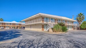 A motel with a two-story structure, a covered parking area, and a small landscaped area with palm trees.