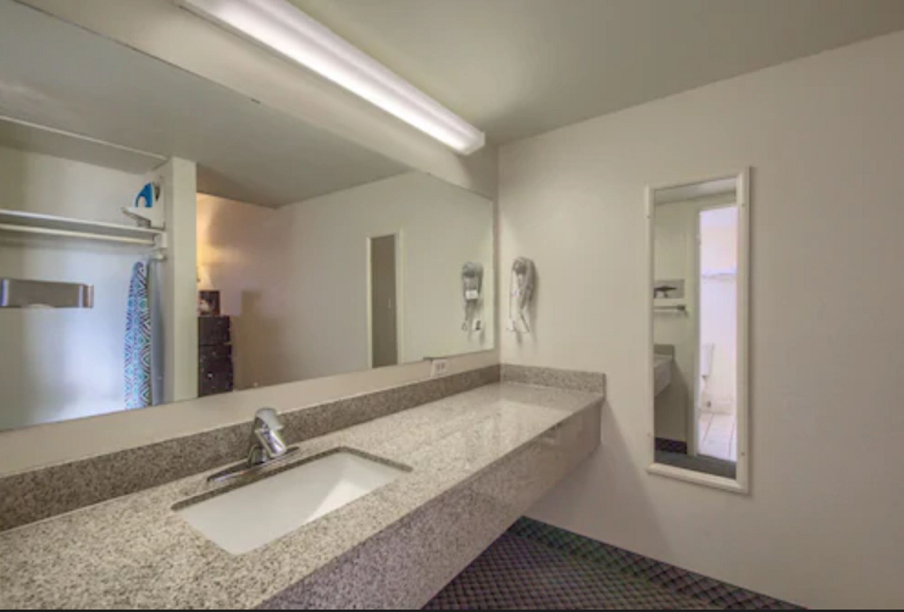 A bathroom with a granite countertop sink, a large mirror, and a towel rack.