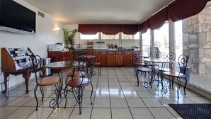 A spacious dining area with a kitchen in the background, featuring a large TV, a buffet setup, and a stone wall. - Americas Best Value Inn Uvalde (Uvalde)