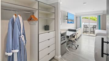 Habitación de hotel con vestidor, un escritorio y silla, zona de comedor con mesa y sillas, y un ventanal con vistas al exterior.