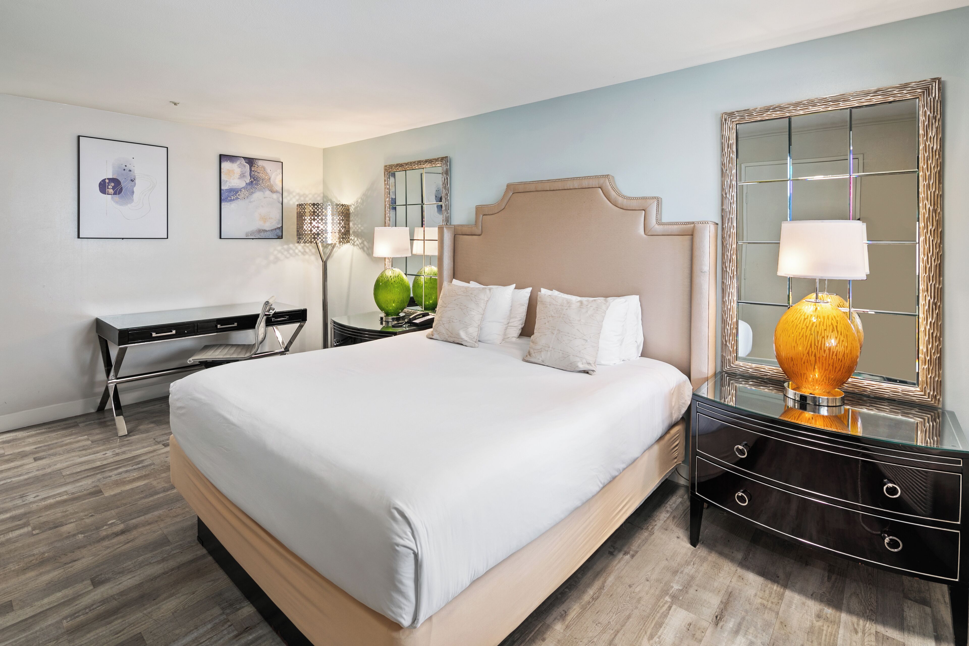 A modern hotel room with a large bed, a desk, a nightstand, and a mirror.